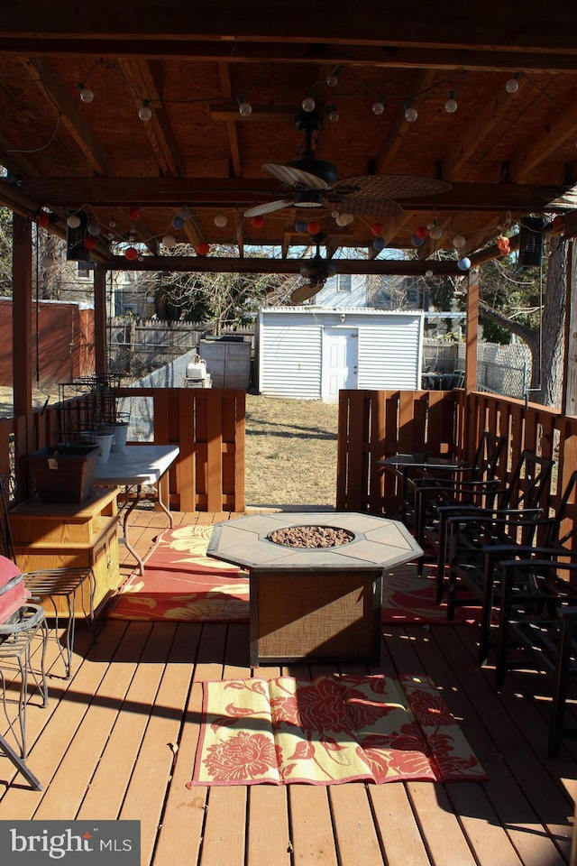 wooden deck with an outbuilding, an outdoor fire pit, a storage shed, fence, and a ceiling fan