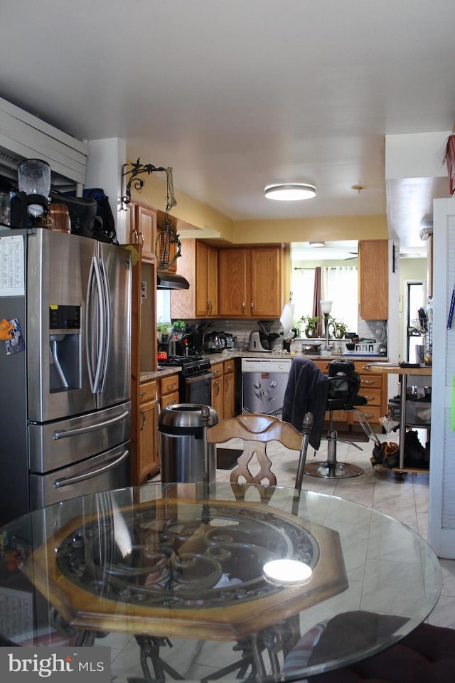 kitchen featuring brown cabinets, decorative backsplash, black range with gas stovetop, stainless steel fridge, and dishwashing machine