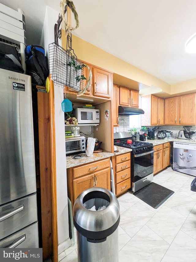 kitchen featuring a toaster, tasteful backsplash, appliances with stainless steel finishes, light stone countertops, and under cabinet range hood