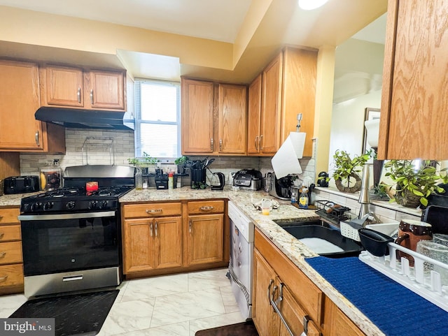 kitchen featuring under cabinet range hood, marble finish floor, dishwasher, brown cabinetry, and stainless steel range with gas stovetop