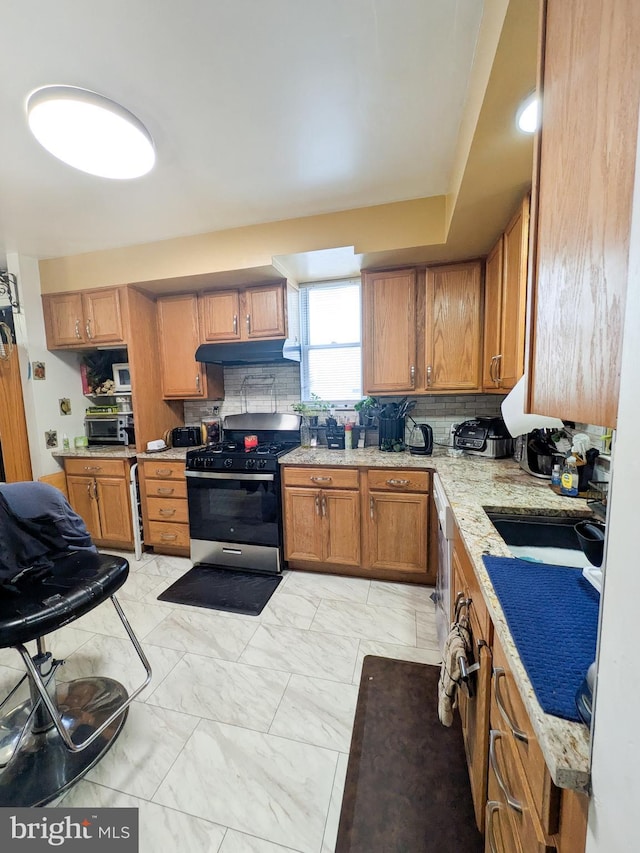 kitchen featuring under cabinet range hood, range with gas stovetop, marble finish floor, brown cabinets, and tasteful backsplash