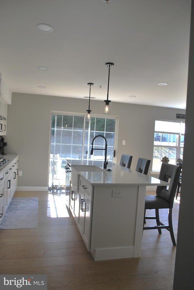 kitchen with light countertops, white cabinets, decorative light fixtures, and light wood-style floors