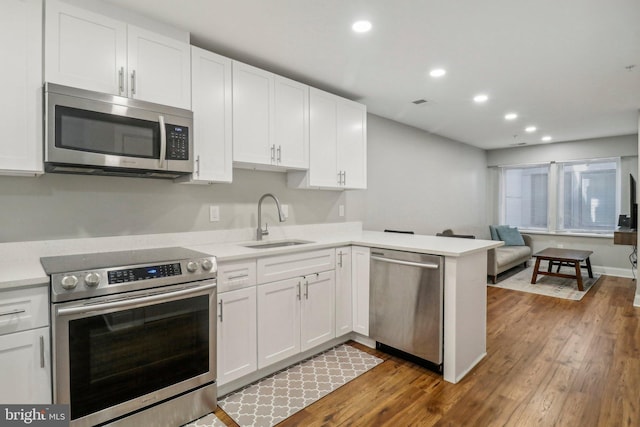 kitchen featuring a peninsula, stainless steel appliances, light countertops, white cabinetry, and a sink