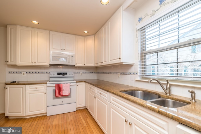 kitchen featuring tasteful backsplash, light wood-style flooring, white cabinets, white appliances, and a sink