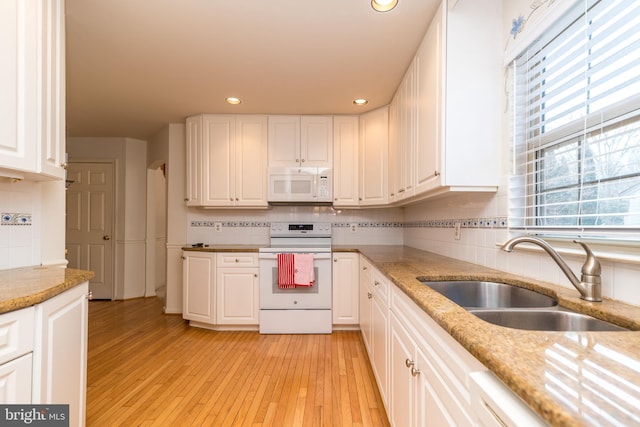 kitchen featuring light wood finished floors, white cabinets, white appliances, and a sink