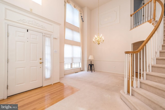 carpeted entrance foyer featuring a notable chandelier, wood finished floors, stairway, a high ceiling, and baseboards