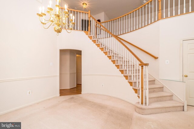 staircase featuring a towering ceiling, baseboards, carpet floors, and a chandelier