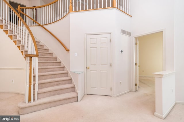 staircase featuring carpet flooring, visible vents, baseboards, and a towering ceiling