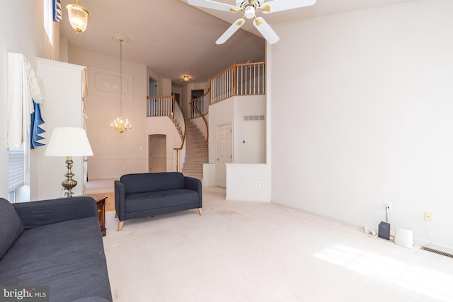 living room with visible vents, stairs, carpet flooring, ceiling fan with notable chandelier, and a high ceiling