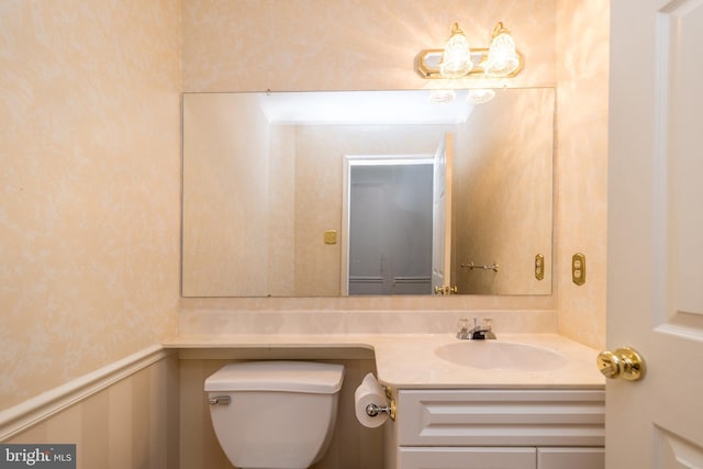 half bathroom featuring vanity, toilet, and wainscoting