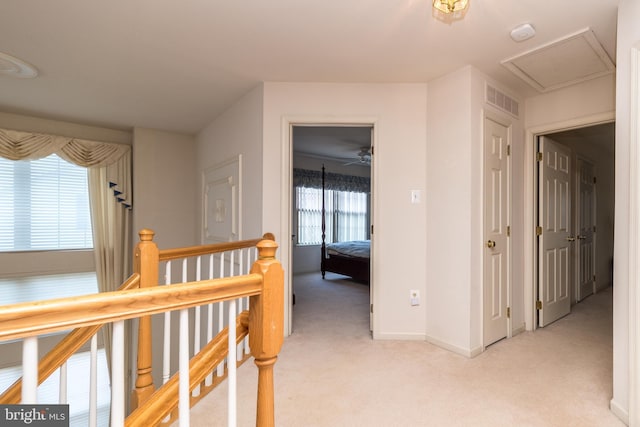 hall with an upstairs landing, visible vents, light carpet, and attic access