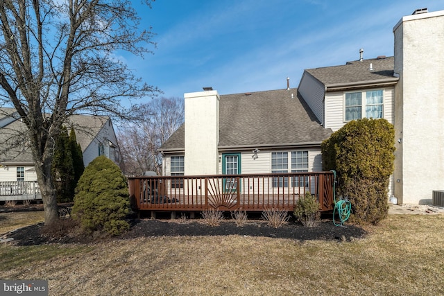 back of property with roof with shingles, a deck, and a chimney