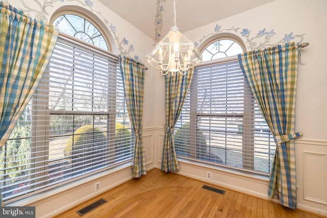 unfurnished dining area with visible vents, a notable chandelier, wood finished floors, and wainscoting