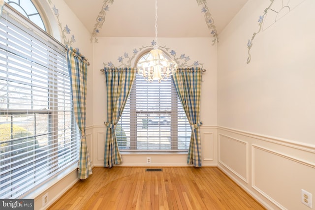 unfurnished dining area featuring an inviting chandelier, light wood-style flooring, plenty of natural light, and visible vents