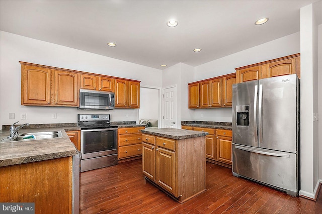 kitchen with appliances with stainless steel finishes, dark wood finished floors, a sink, and a center island