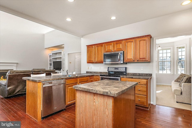 kitchen featuring stainless steel appliances, a peninsula, open floor plan, a center island, and dark countertops