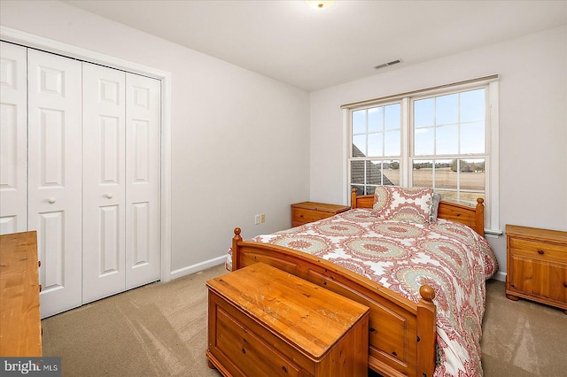 bedroom with baseboards, visible vents, a closet, and light colored carpet