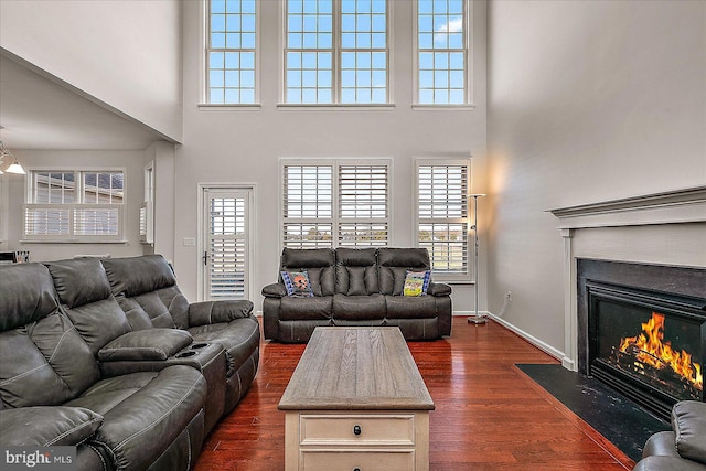 living room with a fireplace with flush hearth, dark wood-style flooring, a towering ceiling, and baseboards