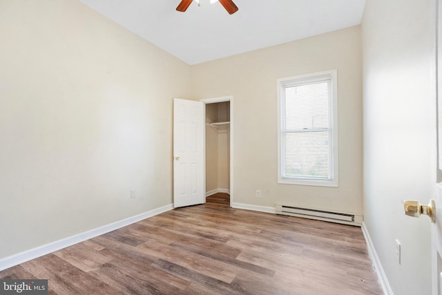 unfurnished bedroom featuring a closet, baseboard heating, ceiling fan, wood finished floors, and baseboards