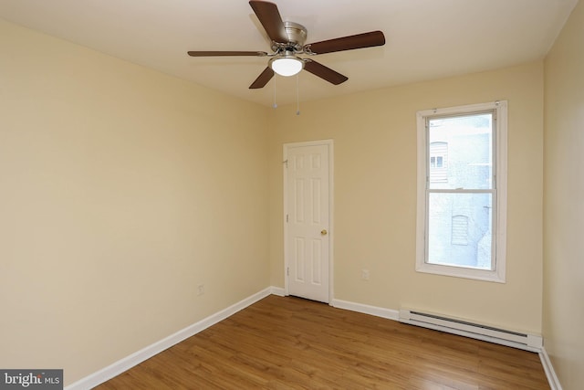 spare room featuring a baseboard heating unit, wood finished floors, a ceiling fan, and baseboards