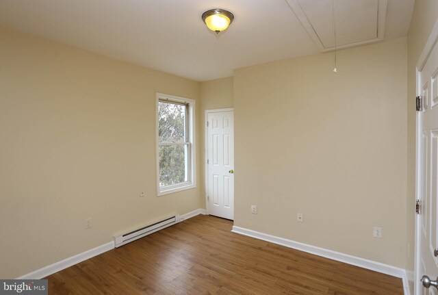 unfurnished bedroom with attic access, baseboards, baseboard heating, and wood finished floors