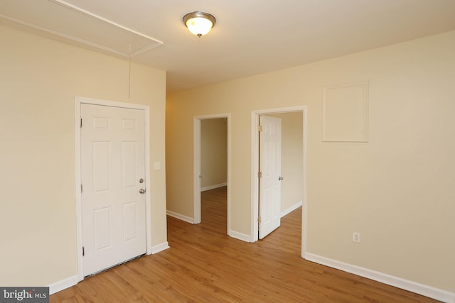 spare room with baseboards, attic access, and light wood-style floors