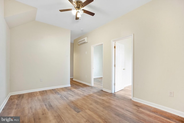 spare room featuring lofted ceiling, a wall mounted AC, ceiling fan, light wood-type flooring, and baseboards