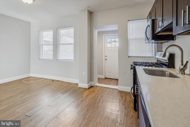 kitchen with dark brown cabinetry, baseboards, light wood-style flooring, light stone countertops, and a sink