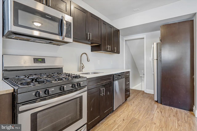 kitchen featuring stainless steel appliances, light countertops, a sink, dark brown cabinetry, and light wood-type flooring