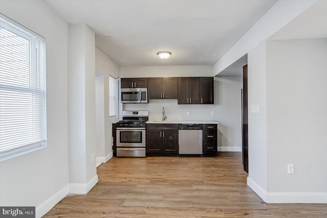 kitchen featuring baseboards, stainless steel appliances, light wood finished floors, and dark brown cabinets