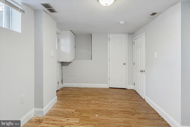 hallway featuring baseboards, visible vents, and light wood finished floors