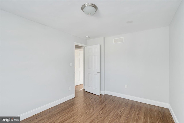 empty room featuring wood finished floors, visible vents, and baseboards