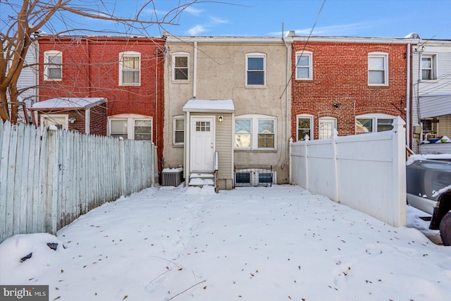 snow covered rear of property with fence private yard, stucco siding, central AC unit, and entry steps