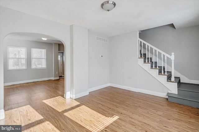 interior space with arched walkways, wood finished floors, visible vents, and baseboards