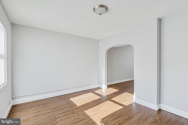 spare room featuring baseboards, arched walkways, and wood finished floors