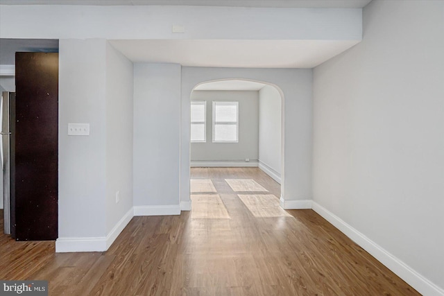 unfurnished room with arched walkways, wood finished floors, and baseboards