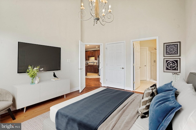 bedroom featuring a towering ceiling, ensuite bathroom, freestanding refrigerator, wood finished floors, and baseboards