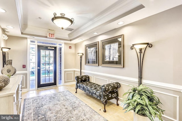 foyer featuring visible vents, a raised ceiling, a wainscoted wall, crown molding, and a decorative wall