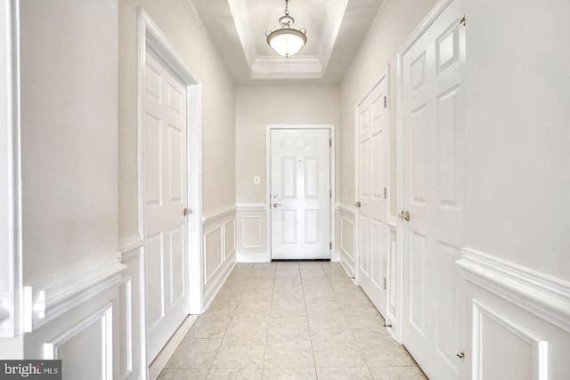 hall featuring a tray ceiling, a wainscoted wall, a decorative wall, ornamental molding, and light tile patterned flooring