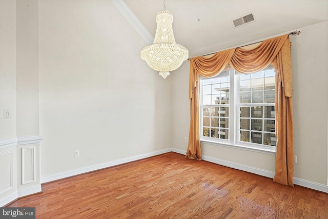 spare room featuring a chandelier, wood finished floors, visible vents, baseboards, and ornamental molding