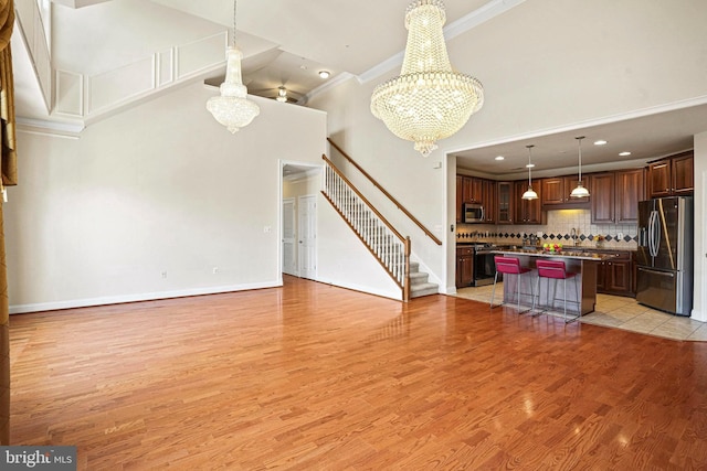 unfurnished living room with light wood-type flooring, stairs, ornamental molding, and a notable chandelier