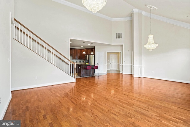 unfurnished living room with visible vents, ornamental molding, an inviting chandelier, stairs, and light wood-style floors