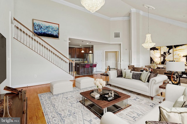 living area featuring visible vents, light wood-style floors, ornamental molding, stairway, and an inviting chandelier