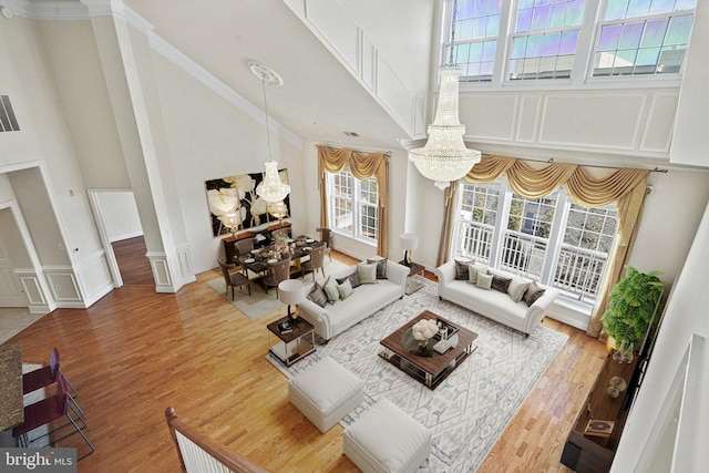 living area featuring a chandelier, wood finished floors, a towering ceiling, and ornate columns