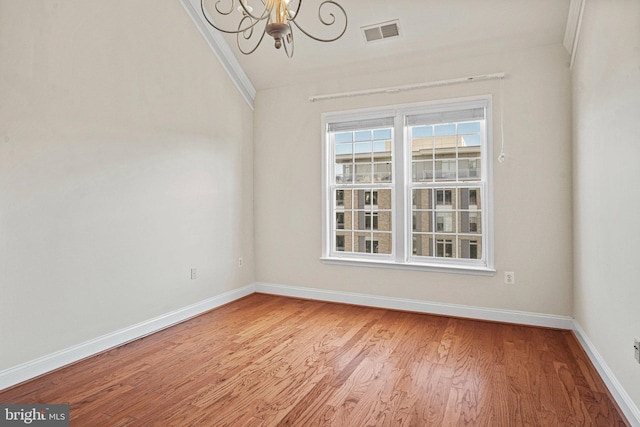 spare room with baseboards, visible vents, a chandelier, and wood finished floors