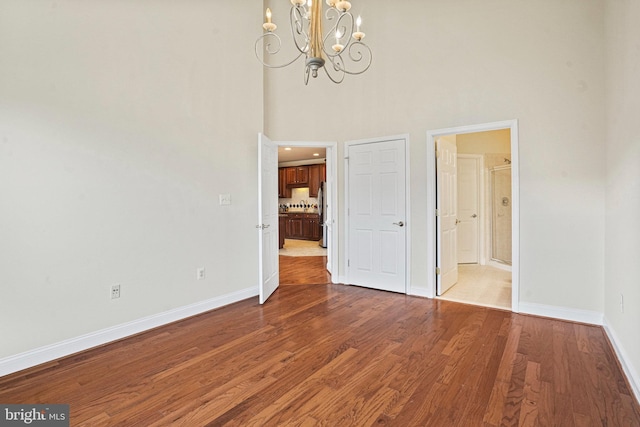 unfurnished bedroom with ensuite bath, baseboards, wood finished floors, and freestanding refrigerator