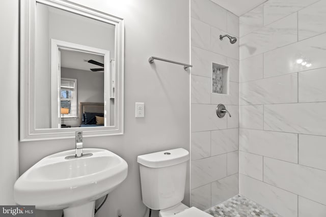 bathroom with tiled shower, a sink, and toilet