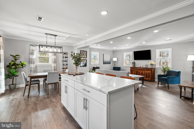 kitchen with ornamental molding, a center island, visible vents, and wood finished floors