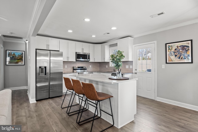 kitchen with stainless steel appliances, tasteful backsplash, visible vents, ornamental molding, and wood finished floors