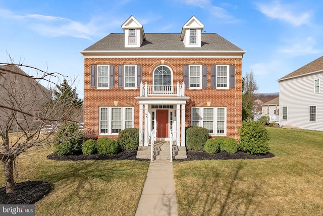 georgian-style home featuring a shingled roof, a front yard, and brick siding